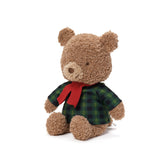 Plush teddy bear wearing a green plaid shirt and red bow tie on a white background