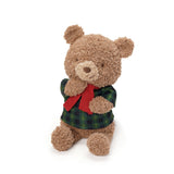 Stuffed teddy bear wearing a plaid shirt and red bow tie on a white background