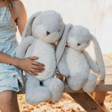 Two large gray plush bunnies held by a person in a light blue dress.