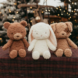 Two brown plush friends and a white rabbit plush toy on a checkered surface with a blurred festive background.