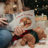 Person reading 'A Sweet Tradition' book to a child with teddy bears around, festive background.