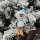 Decorative penguin ornament with a blue hat and scarf hanging on a frosty branch.