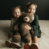 Two children holding a teddy bear on a soft surface with a dark background