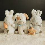 Three plush toys resembling a rabbit, a dog, and another rabbit on a soft surface with a dark background.