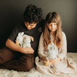 Two children sitting on a carpeted floor holding stuffed animals.