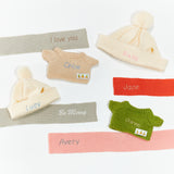 Collection of small knitted sweaters and hats with embroidered names on a white background