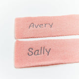 Two pink scarves with embroidered names 'Avery' and 'Sally' on a white background