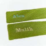 Two green scarves with embroidered names 'Alex' and 'Malik' on a white background