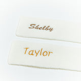 Two white scarves with embroidered names 'Shelby' and 'Taylor' on a light gray background.