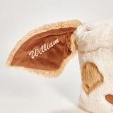 Close-up of a plush toy with a brown ear embroidered with 'William' on a light gray background