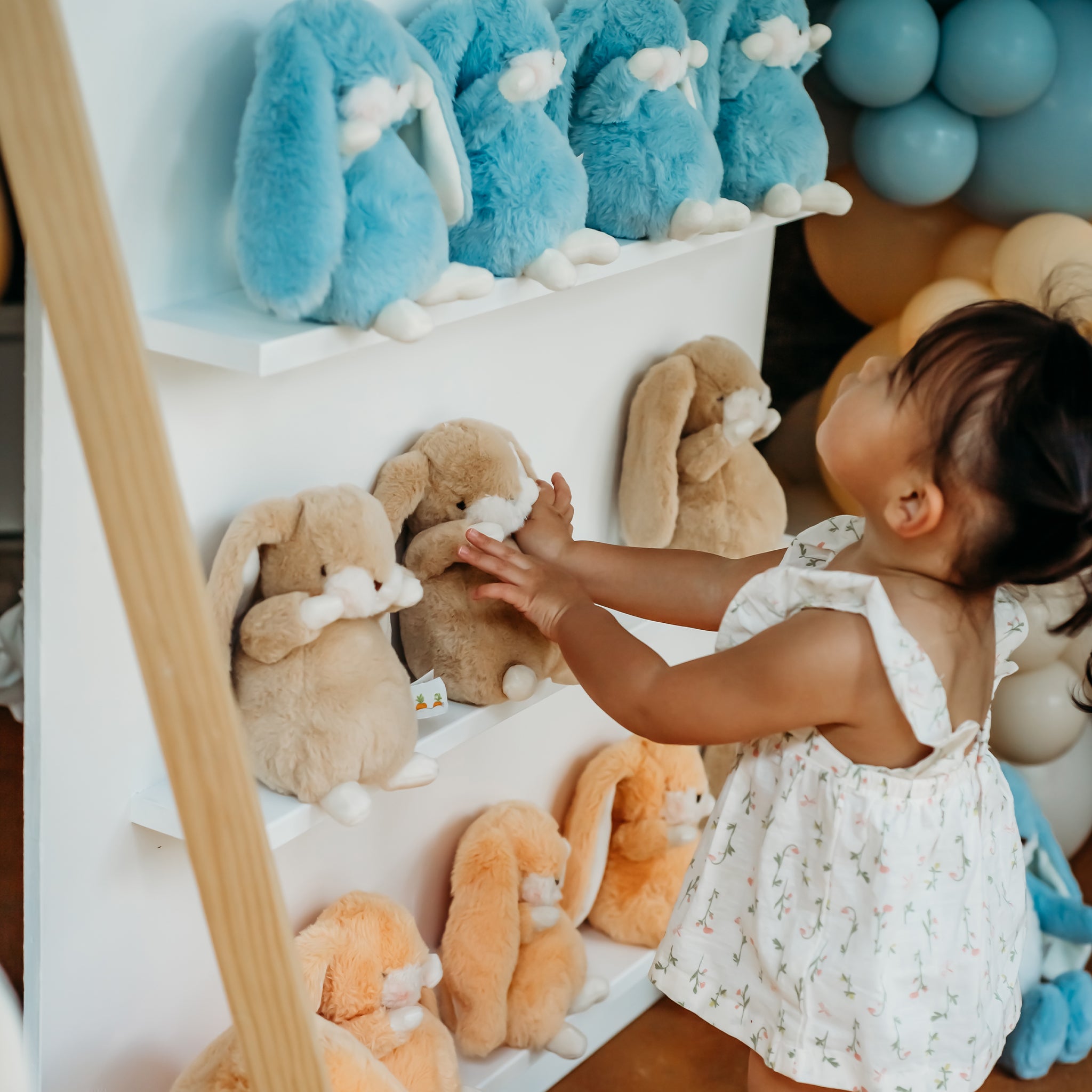 Child playing with plush bunny toys in a display case, surrounded by balloons and other toys.
