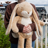 Person holding a large beige plush bunny in an outdoor setting