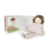 Stuffed doll in a pink dress with a book featuring a girl and bird illustration on a white background