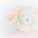 A close-up of a white plush bunny comforter or stuffed toy with long floppy ears, one ear embroidered with the name 'Maddy' in pink, wearing a light pink tulle skirt against a plain white background.