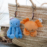 Two plush keychains, one blue and one orange, hanging from a straw bag.