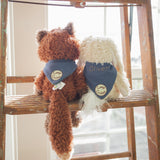 Fox and bunny stuffed animals, one brown and one white, sitting on a wooden ladder with 'Oliver' embroidered one one of their bandanas.