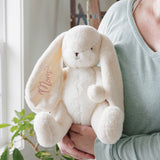 Person holding a plush bunny toy with 'Mom' on its ear in a home setting.