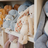 Group of plush bunnies on a white shelf, in cream blue and orange colors.