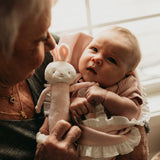 A grandmother holding her grandchild and a pink bunny rattle.