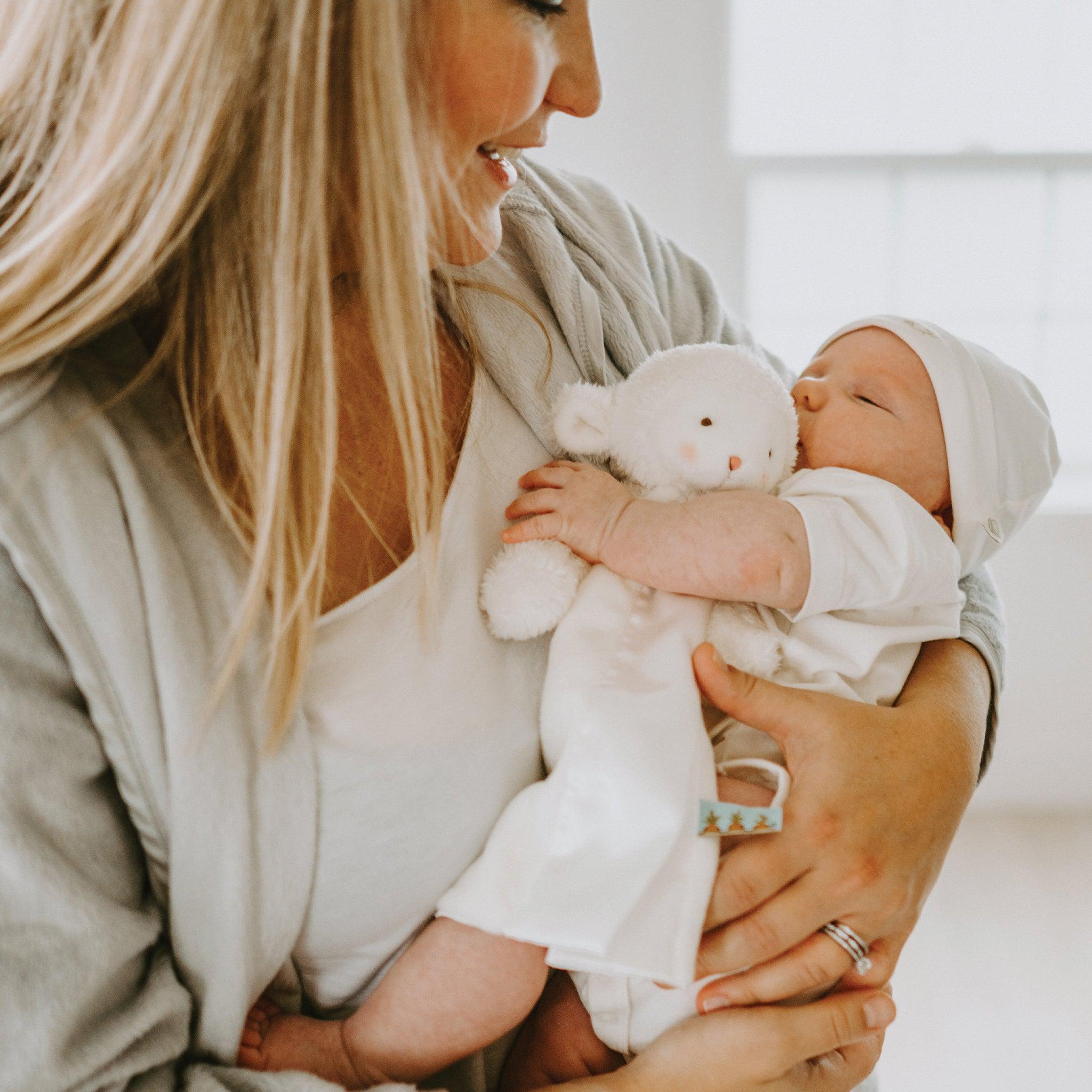 Mother holding baby in white outfit, baby is holding a white lamb lovey