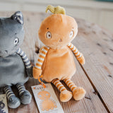 A plush orange character doll with striped yellow-and-white arms and legs sits on a wooden surface next to a gray cat plush toy. A small paper tag with the brand name Hutch Studio is visible in front.