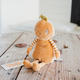 A plush pumpkin doll toy with orange fabric, striped yellow and white arms and legs, and a small green stem on its head, sitting on a rustic wooden table.