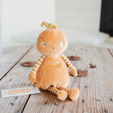 A plush toy shaped like a round orange character with striped orange-and-white arms and legs, sitting on a rustic wooden table.