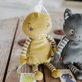Two handmade plush toys sitting on a rustic wooden surface. The toy on the left is a round green monster creature with striped arms and legs, and a small white tuft on its head.