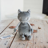 A gray plush cat toy with striped arms and legs, sitting on a rustic wooden table.