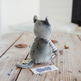 A gray plush cat toy with striped arms and legs, shown from behind sitting on a rustic wooden table.