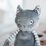 A close-up of a gray plush cat toy with striped blue and white arms, photographed against a softly blurred light background.