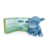 Blue hippo plush toy next to an open book with hippo illustrations on a white background