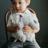 Child holding a gray stuffed elephant toy against a dark background
