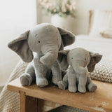 Two plush elephant toys on a wooden surface with a soft, blurred background.