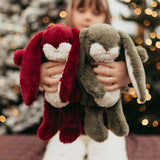 Child holding two plush bunny toys against a blurred festive background