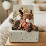 Two stuffed animals, a reindeer and a mouse, wearing scarves, on a decorative box with a blurred indoor background.