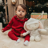 Child in a red outfit sitting next to a white plush toy with Christmas decorations in the background.
