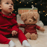 Child in red outfit with teddy bear wearing a sweater in a festive setting
