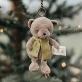 Teddy bear keychain with a green scarf and tag hanging on a tree