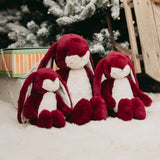 Three red and white plush bunnies sitting together with a Christmas tree and decorations in the background.