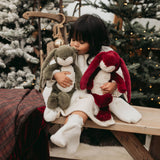 Child holding two plush bunny toys in a festive outdoor setting with Christmas trees.