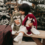 Child holding two plush toys in a festive setting with Christmas trees.