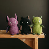 Three colorful plush monsters on a wooden surface with a dark background