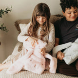 Two children sitting on a couch holding plush toys.