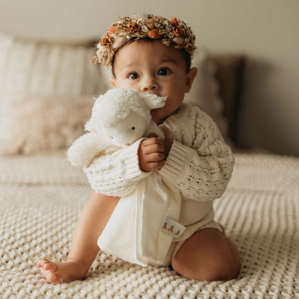 Baby holding white lamb lovey on a textured background.