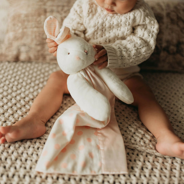 Baby holding a plush bunny toy on a textured surface