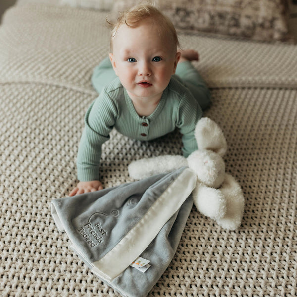 Baby in a green outfit lying on a textured surface with a soft toy.