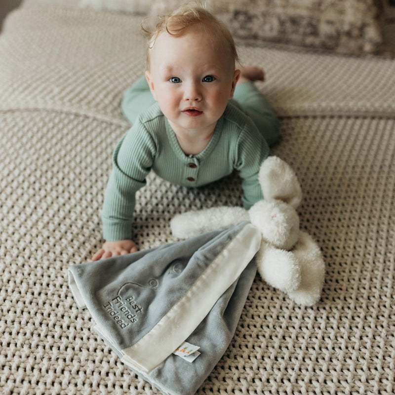 Baby in a green outfit lying on a textured surface with a soft toy.
