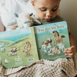 Child holding a book titled 'You Are My Baby' with farm animal illustrations.