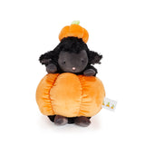 A plush toy featuring a black sheep sitting on a large orange pumpkin, with a small orange pumpkin hat on its head, photographed on a clean white background.